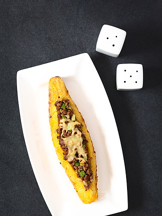 烤熟的<i>车</i><i>前</i>草，里面塞满肉末、橄榄、青椒和洋葱，撒上奶酪，这是中美洲的一道传统菜肴，叫做 Canoa de Platano（<i>车</i><i>前</i>草独木舟），在自然光下在石板上拍摄