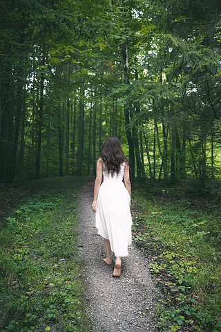 一个年轻的黑发女人的背影,穿着优雅的白色连衣裙,赤脚走在穿过春天