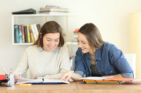 两个快乐的学生一起学习的正面肖像，互相帮助，在桌子上的笔记本上阅读笔记