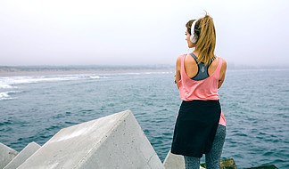 戴着耳机看海的女运动员的背影。戴着耳机看海的女运动员
