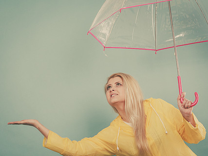 穿著黃色雨衣的金髮女人拿著透明雨傘在下雨時檢查天氣.