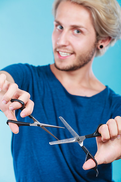 热情的男性理发师拿着剪刀展示工作工具正常和变薄的剪刀