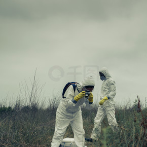 身穿细菌防护服的妇女为一具尸体拍照，她的伙伴在后台检查该地区。穿着细菌防护服的男女给尸体拍照