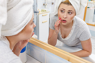 担心震惊的女人看着镜子里的倒影，想着她的脸庞表情严肃，分析面部皮肤肤<i>色</i>。女人看着镜子里的倒影