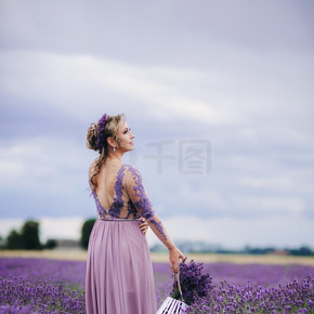 美丽浪漫的女人在薰衣草田里走着紫色薰衣草花篮的肖像，夏日。美丽浪漫的女人在薰衣草田里带着紫色薰衣草花篮行走的肖像，夏日