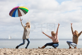 三个女人开心地打着五颜六色的伞跳来跳去。女性朋友在户外玩得开心。女性用雨伞玩得开心