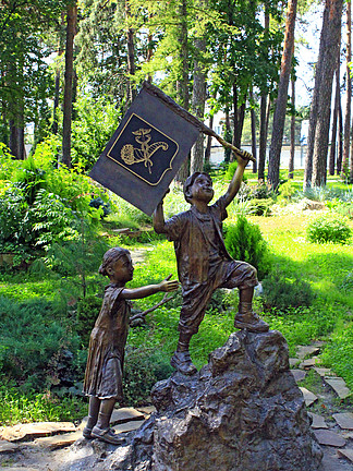 带国旗的小男孩和女孩在城市公园上山的青铜雕塑。哈尔科夫市公园儿童纪<i>念</i>碑。城市公园小男孩带旗女孩上山铜像