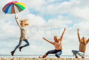 三个女人开心地打着五颜六色的伞跳来跳去。女性朋友在户外玩得开心。女性用雨伞跳跃