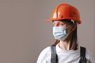 灰色背景中戴着医用面具和橙色建筑头盔的漂亮女工。职业安全与健康专家，戴着冠状病毒 <i><i>covid</i></i>-19 面罩。灰色背景中戴着医用口罩和橙色建筑头盔的漂亮女工。带有冠状病毒<i><i>covid</i></i>-19面罩的职业安全和健