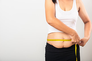 亚洲母亲妇女使用部分产后疤痕测量腰部妊娠纹松弛下腹部皮肤她在<i>怀</i><i>孕</i>婴儿出生后肥胖孤立在白色背景下，健康腹部多余身体概念