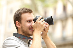 一个快乐的男人在城市或城镇的街道上用 dslr 相机拍照的侧视图