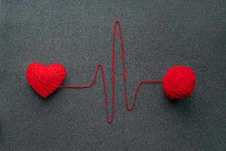 手工制作的红纱球，心由红色羊毛纱和线制成，如灰色羊毛织物背景上的心电图图案。红色温暖的心像爱情的象征。心脏健康、心跳、感觉、爱情、浪漫概念