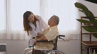 女护士医生穿着白色制服的心脏病专家在坐在轮椅上用听诊器在家检查病人的老人或老人时检查心跳，健康访客的概念