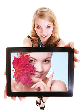 快乐的金发女孩展示 ipad 与红叶和保湿霜的女人的照片。现代年轻女商人拿着平板电脑触摸板推荐护理干<i>性</i><i>皮</i>肤。孤立。科技与美。