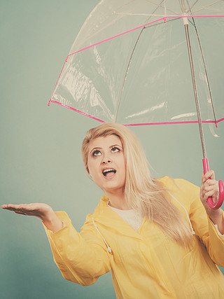 穿著黃色雨衣的金髮女人拿著透明雨傘在下雨時檢查天氣.