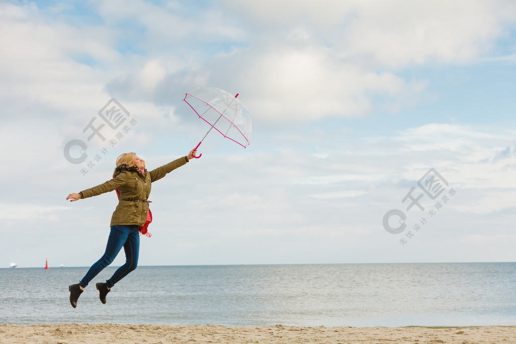 女人在海邊,陽光明媚的日子和清澈的藍天上用透明雨傘跳躍.