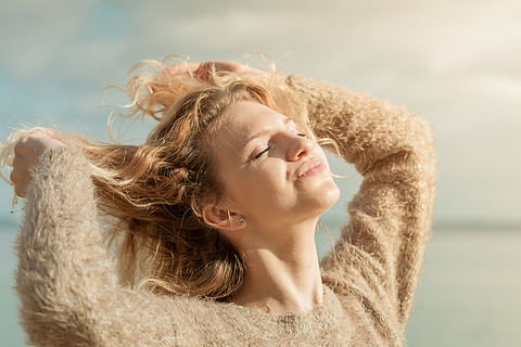 快乐的女性积极地在户外行走,穿着毛衣,在阳光下头发被风吹乱,户外穿