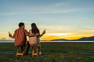 相爱的年轻夫妇在日落时分坐在草地上聚会