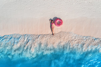 鸟瞰美丽的年轻躺着的<i>女</i><i>人</i>，戴着粉色甜甜圈游泳圈，在海边的白色沙滩上，日落时分海浪。暑假。苗条<i>女</i>孩的顶视图，湛蓝的水。印度洋