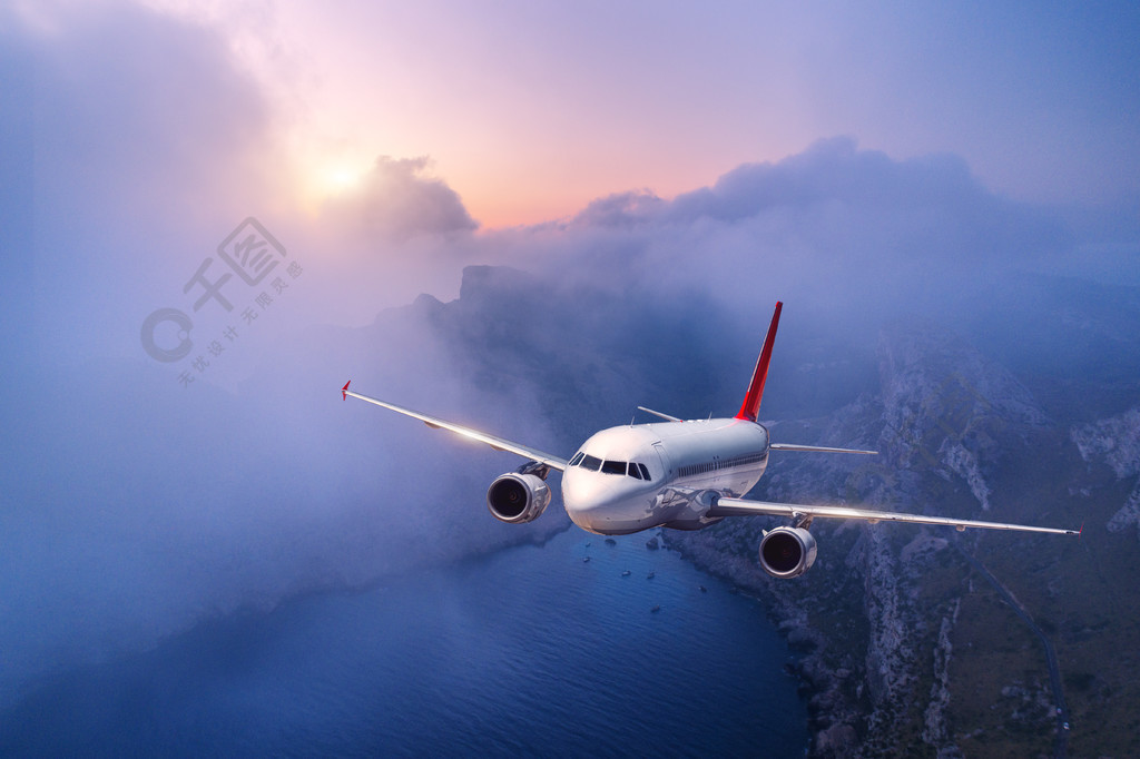客机在日落时分飞过云层景观与白色飞机低云海岸黄昏紫色的天空飞机