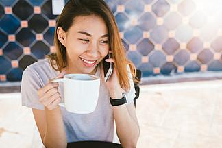 快乐的微笑亚洲女商人使用会<i>说</i><i>话</i>的手机坐在。快乐的微笑亚洲商界女性使用会<i>说</i><i>话</i>的手机坐在咖啡馆里，拿着一杯咖啡。美丽开朗的亚洲女人在咖啡馆谈电<i>话</i>，一边享受咖啡一边微笑。