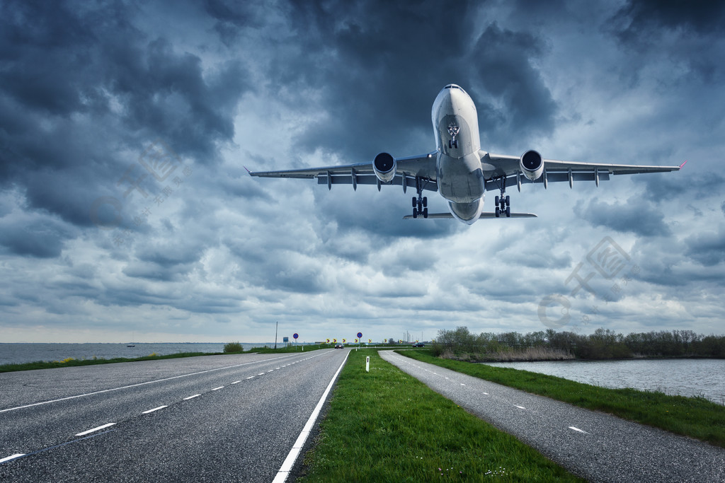 在柏油路和草地上空在多雲的天空中飛行客機正在跑道上著陸商用飛機