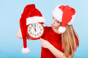 圣诞节，季节性服装，圣诞节时间概念。穿着圣诞老人帮手服装的幸福女人拿着大红钟，等待庆祝。穿着圣诞老人服装的快乐女人拿着时钟
