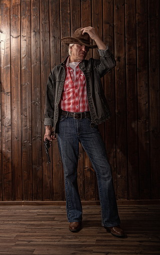 穿着古典的中年牛仔拿着左轮手枪站在一间有木墙的黑暗房间里