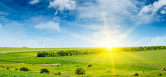 丘陵绿地、太阳升起和风<i>车</i>在蓝天背景。农业景观。宽幅照片。
