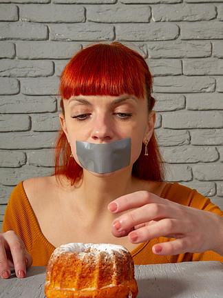 一个年轻的红发女孩节食的概念形象，她的嘴在开胃糕点前用银胶带<i>粘</i>住。减肥唇膏