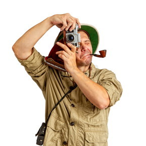 成年游客戴着热带软木头盔，身穿防护服，嘴里衔着一根管子，用旧相机拍照。热带头盔旅游