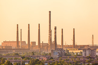 钢<i>厂</i>背景上的城市建筑，在五颜六色的日落时有烟囱。冶金<i>厂</i>。钢铁<i>厂</i>，钢铁<i>厂</i>。欧洲的重工业。烟囱造成的空气污染。产业格局