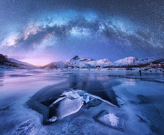 挪威罗弗敦群岛冬季夜间冰冻海岸和<i>雪</i>山上的银河。与蓝色星空、 水、 冰、 白<i>雪</i>皑皑的岩石、 银河系的北极景观。太空和银河