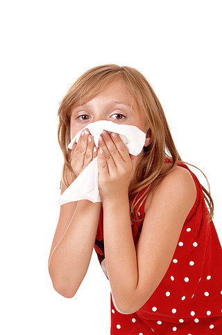 一个可爱的年轻金发女孩在她流鼻涕的鼻子上拿着纸巾,因白色背景而被