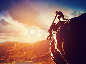 登山者在岩石上攀登，日落时分的山上，其中一个人伸出手，帮助攀登。在危险情况下提供帮助、支持、协助