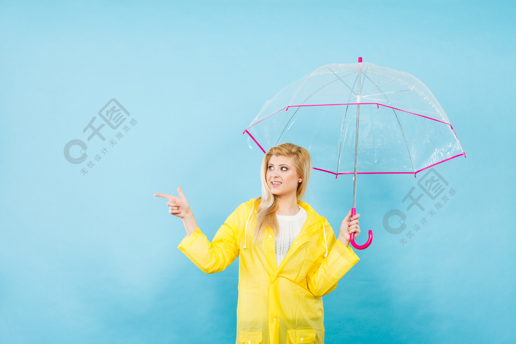 金髮女人穿著黃色雨衣拿著透明雨傘檢查天氣是否下雨用手指指著複印