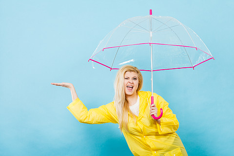 穿著黃色雨衣的金髮女人拿著透明雨傘在下雨時檢查天氣.