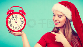 圣诞节，季节性服装，圣诞节时间概念。穿着圣诞老人帮手服装的幸福女人拿着大红钟，等待庆祝。穿着圣诞老人服装的快乐女人拿着时钟