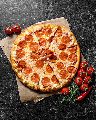 番茄和迷迭香纸上的意大利辣香肠披萨。在黑<i>暗</i>的乡村背景上。番茄和迷迭香纸上的意大利辣香肠披萨。