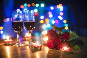 情人节晚餐浪漫爱情概念/浪漫餐桌布置，装饰着情侣香槟酒杯和玫瑰花，烛光在木桌晚餐五颜六色的光散景背景上