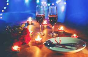 情人节晚餐浪漫爱情概念/浪漫餐桌布置，盘子上装饰着红心叉勺，晚上木桌晚餐上用烛光装饰一对香槟玻璃酒玫瑰