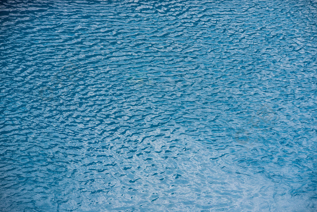 蓝色纹理背景的游泳池上带小波浪和雨滴的水