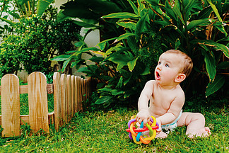宝宝赤脚坐在草坪上玩着五颜六色的玩具来刺<i>激</i>他的感官。