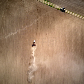 拖拉机犁春田的鸟瞰图，乌克兰拖拉机后面延伸着一列灰尘。无人机拍摄的照片。农业工作春季开始时带种子中耕机的空中观察拖拉机