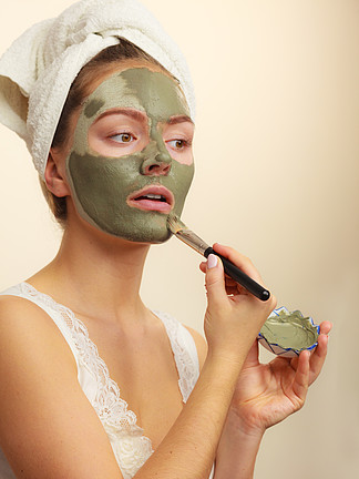 皮肤护理。女人用刷子粘土泥面膜涂在脸上。照顾油性肤<i>色</i>的女孩。美容治疗。用刷子粘土泥面膜涂在脸上的女人