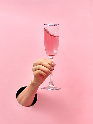 假日概念从墙上的洞里,女性手中的玫瑰酒杯