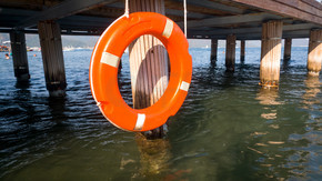 橙色救生圈挂在海滩上的木码头上的特写照片。海边木码头上挂着橙色救生圈的特写图