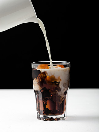 将新鲜牛奶倒入一杯黑咖啡中，白板和黑色背景上有冰块。
