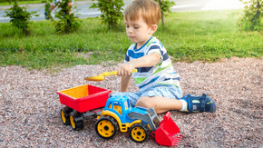 可爱的小男孩在游乐场上玩玩具的特写照片。孩子玩卡车、挖掘机和拖车。他假装是一名建筑工人或司机。可爱的小男孩在游乐场上玩玩具的特写镜头。孩子玩卡车、挖掘机和拖车。他假装是一个建筑商或司机