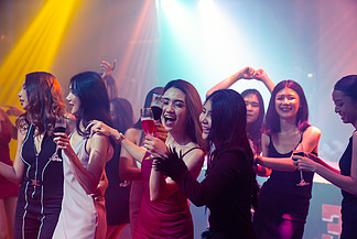 庆祝聚会、喝酒和跳舞的年轻人。一群朋友在晚上在迪<i>斯</i>科俱乐部玩乐的同时敬酒。友谊和夜生活的概念。
